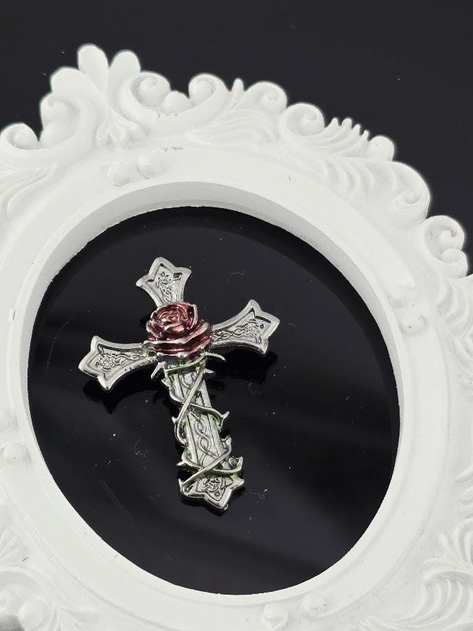 A silver cross brooch with a red rose is displayed in a white box, accompanied by a brown gift box with a red ribbon.