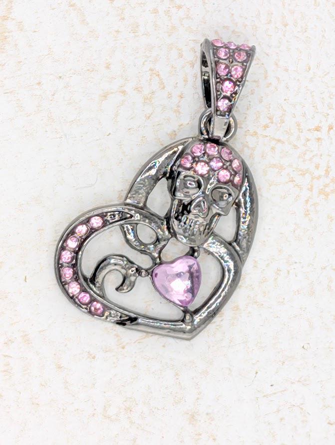 A silver-colored pendant with a heart-shaped design and a skull-shaped design, both adorned with pink gemstones.