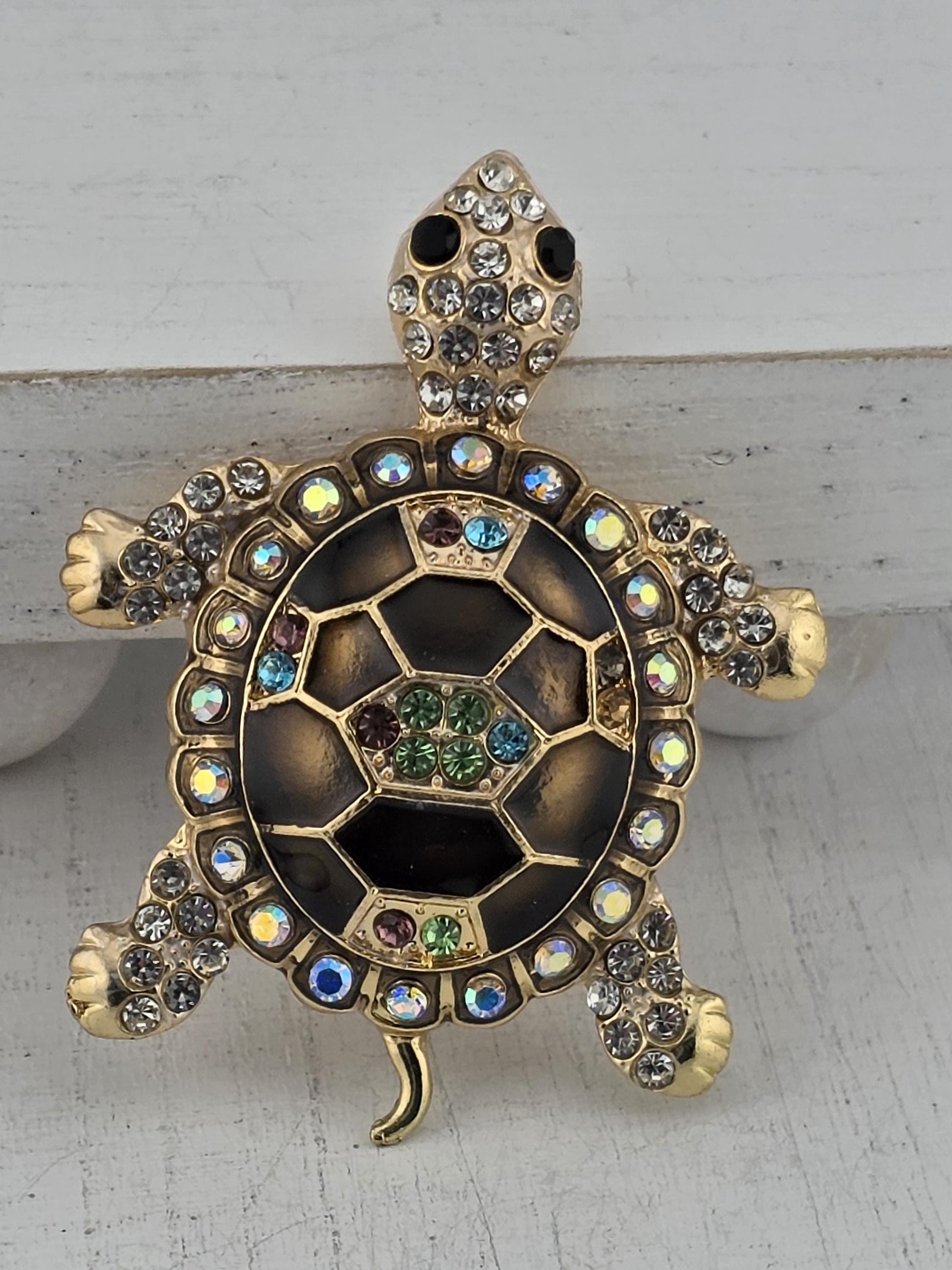 A decorative turtle brooch with a black and gold color scheme, adorned with colorful gemstones.