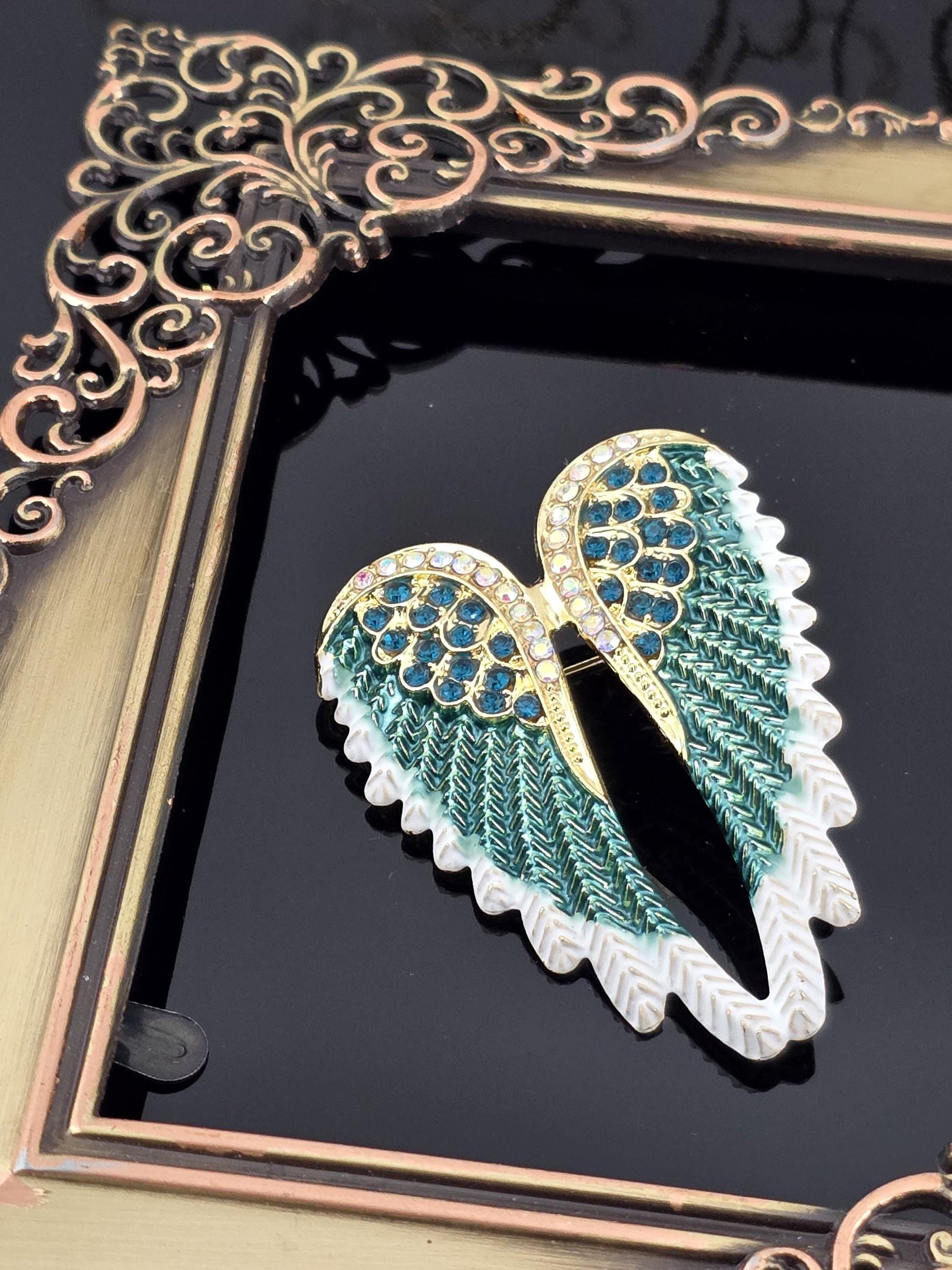 A decorative frame with a gold frame and a black background, featuring a close-up view of a decorative wing-shaped object with blue and green gemstones.