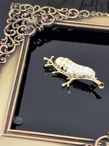a decorative gold-colored pendant or brooch with a white and gold design, displayed within an ornate gold-colored frame.