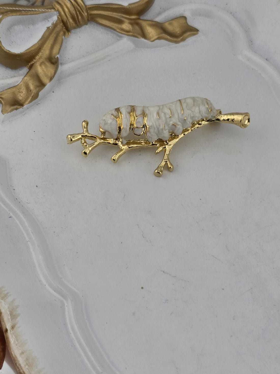 a decorative gold-colored pendant or brooch with a white and gold design, displayed within an ornate gold-colored frame.