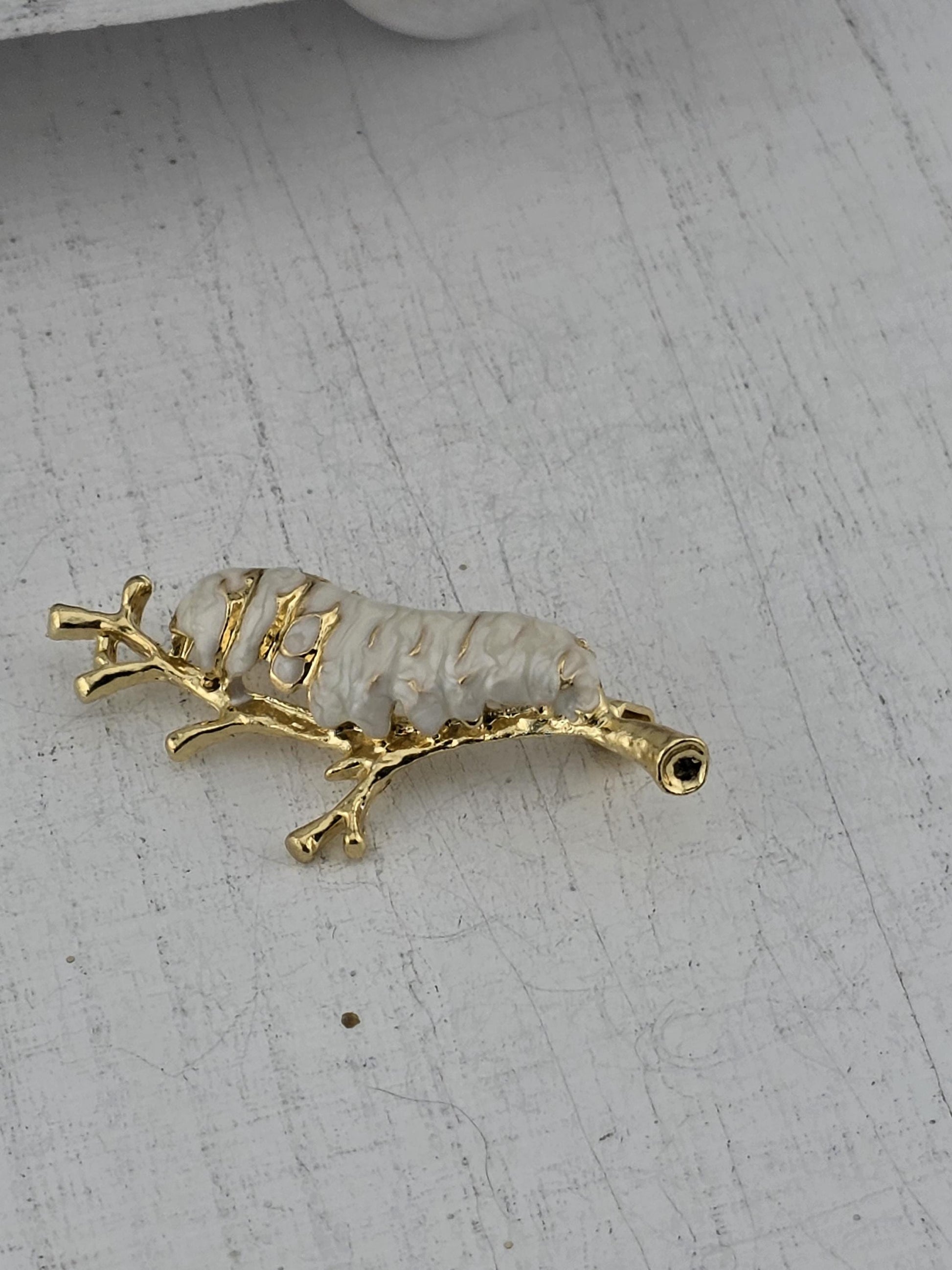 A gold-colored pendant in the shape of a white sea slug or sea slug-like creature, with a small black eye-like feature on top.