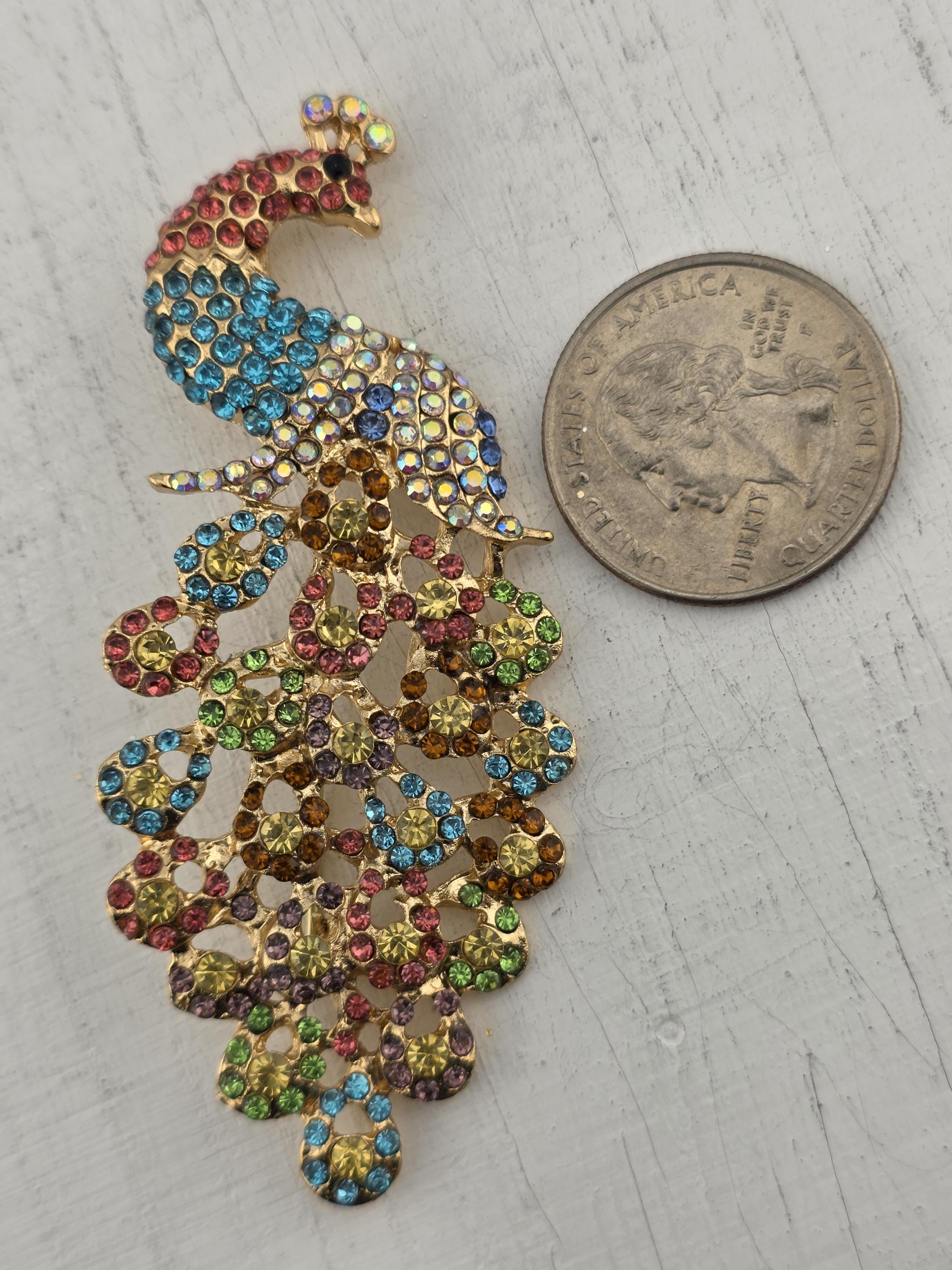 A colorful, sparkling rhinestone brooch is placed next to a United States quarter coin on a white surface.