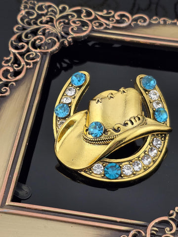 A decorative gold brooch with a blue gemstone and white gemstone accents, placed on a black background within an ornate frame.