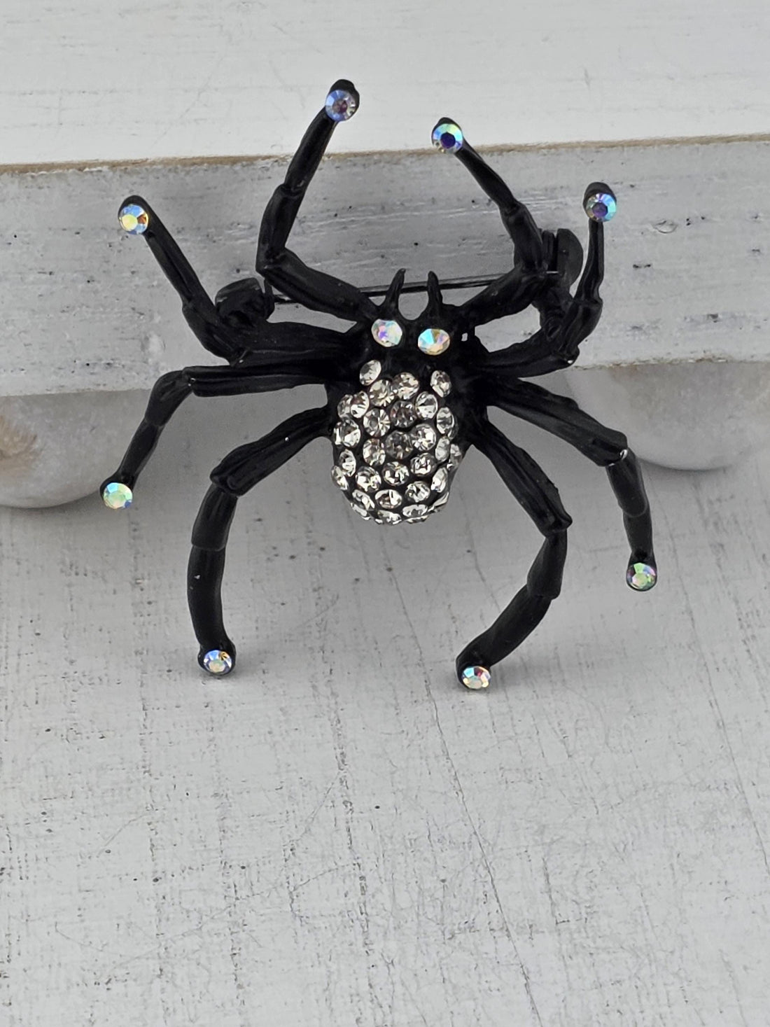 A black spider with rhinestones on its body is displayed against a white background.