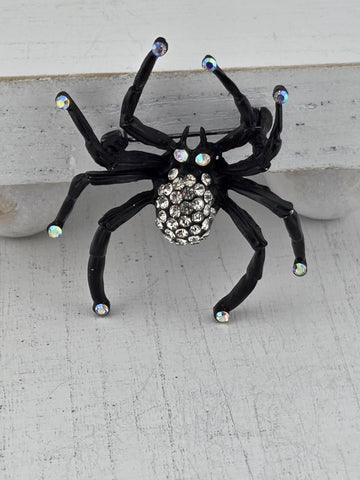 A black spider with rhinestones on its body is displayed against a white background.