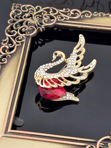 A decorative gold-framed picture with a swan-shaped brooch featuring a red gemstone on its beak.