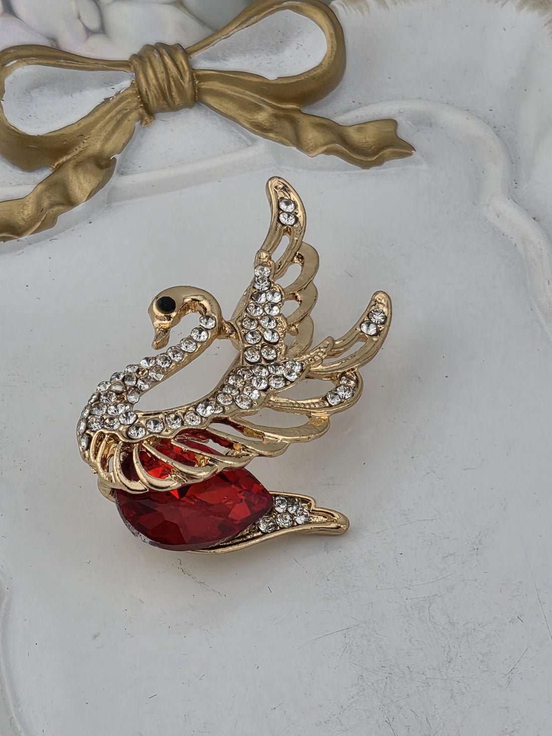 A decorative gold-framed picture with a swan-shaped brooch featuring a red gemstone on its beak.
