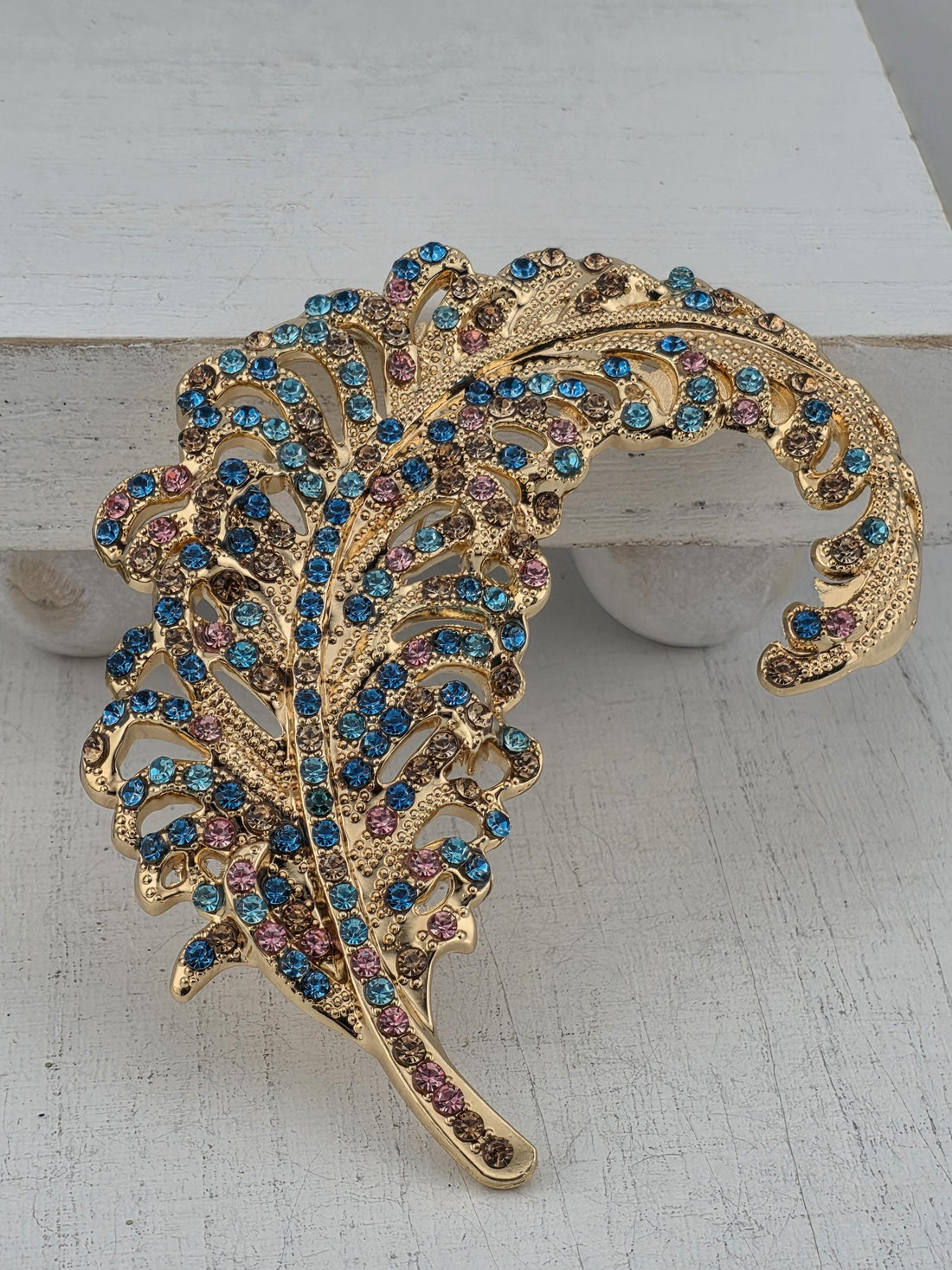 A decorative gold-colored brooch with a feather-like design and colorful gemstones.