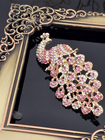 A decorative gold and black frame with a large, ornate peacock brooch with pink and white gemstones.