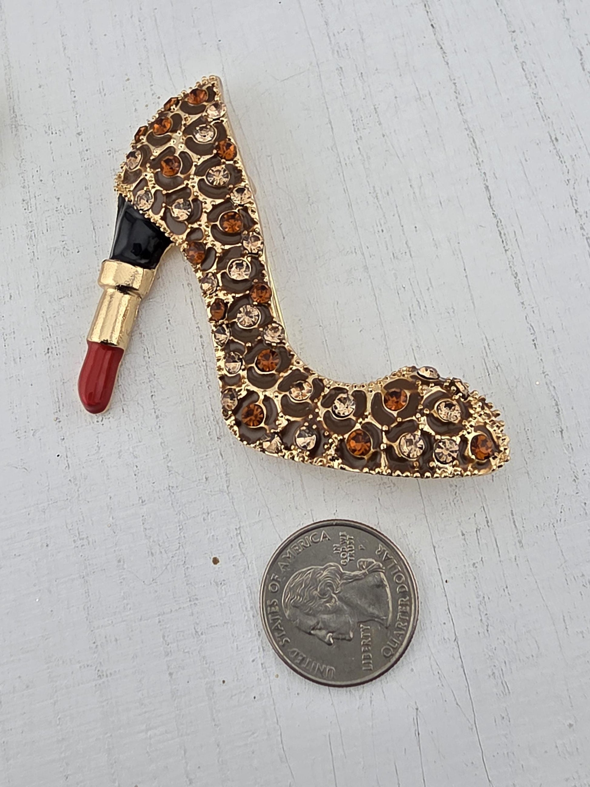 a gold-colored brooch with a red lipstick design, placed next to a United States quarter on a white surface.