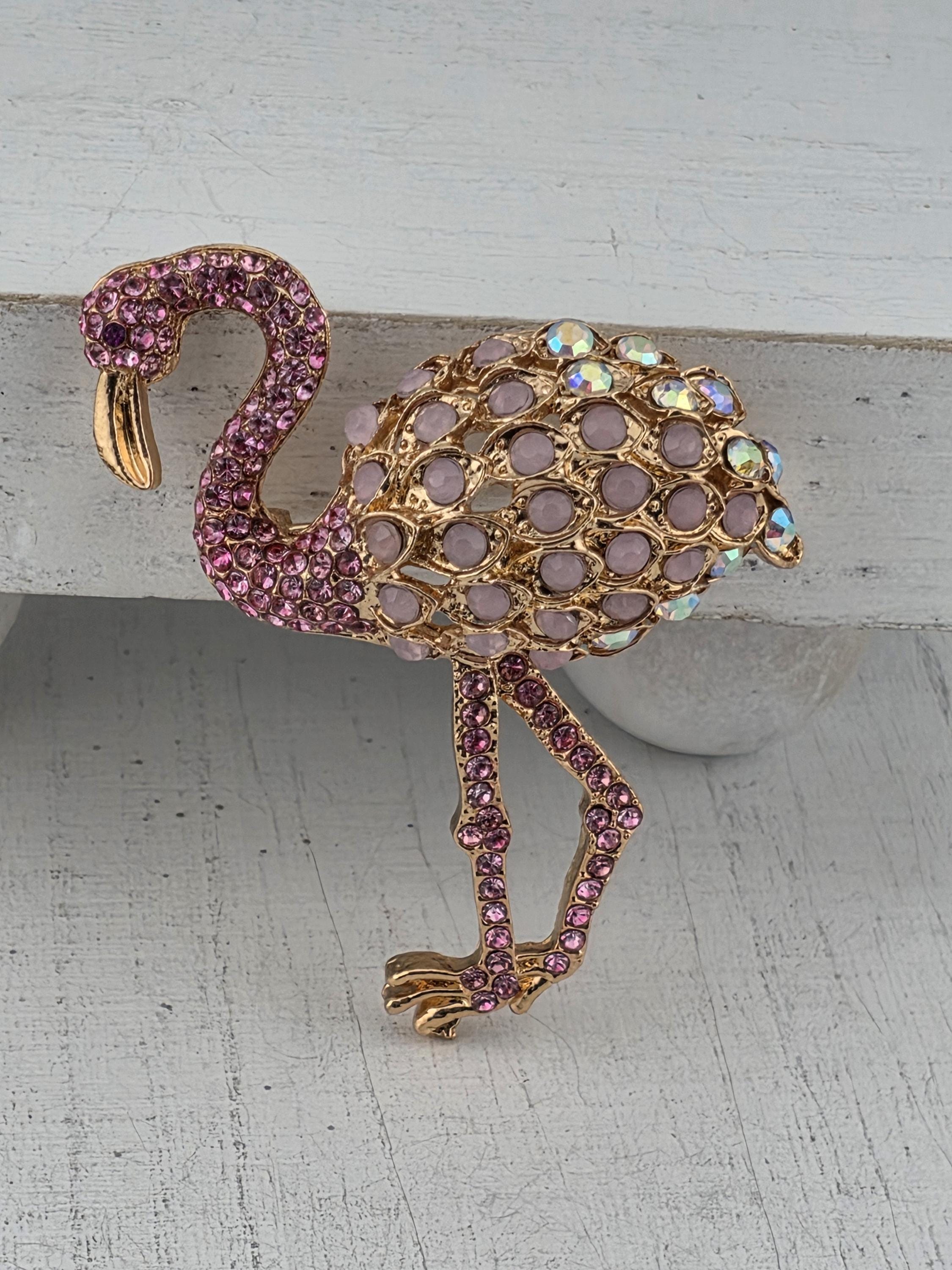 A decorative brooch in the shape of a flamingo, adorned with numerous small, round, purple gemstones.