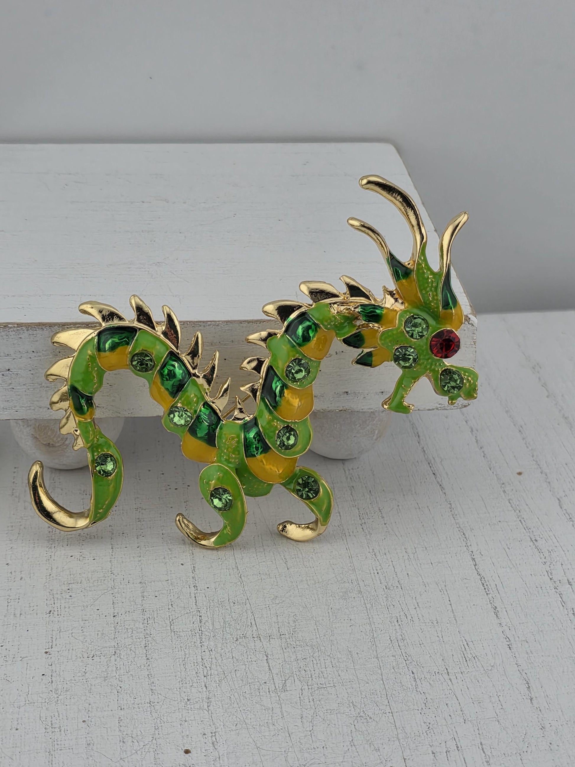 A decorative dragon-shaped brooch with green and yellow colors and sparkling gemstones.