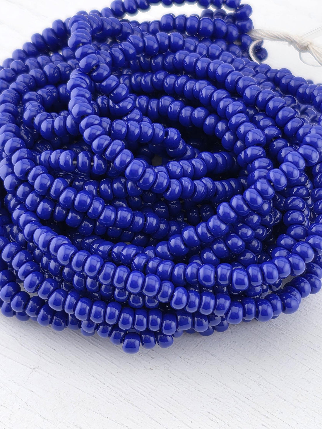 A large pile of blue beads, possibly made of glass or plastic, arranged in a circular pattern on a white surface.