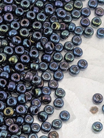 a large pile of multicolored beads, including black, blue, and green beads, scattered on a surface.