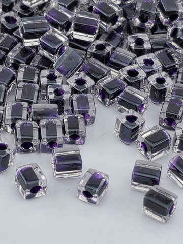 a close-up view of numerous clear glass beads with purple accents, scattered across a white surface.