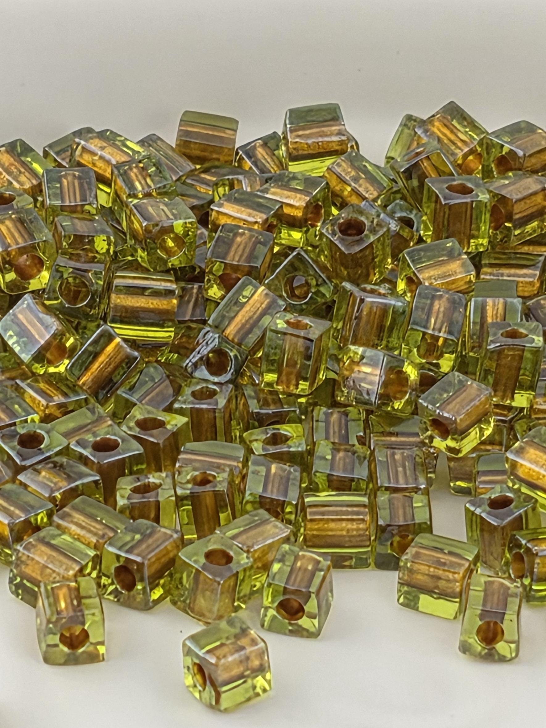 a close-up view of numerous small, clear glass beads in various shades of green and yellow, scattered and overlapping each other.