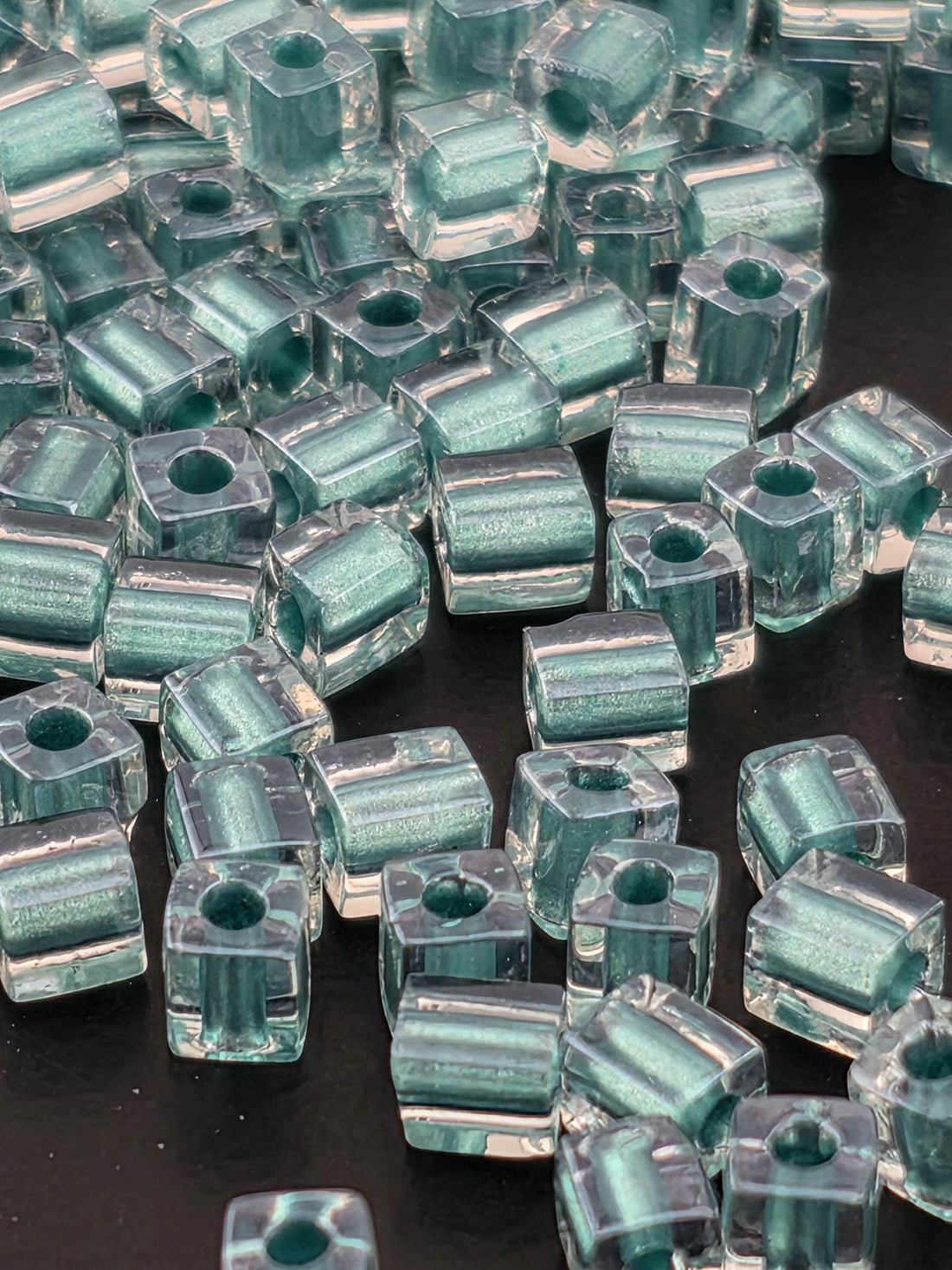 numerous transparent glass beads in various shades of blue and green, scattered across a dark background.
