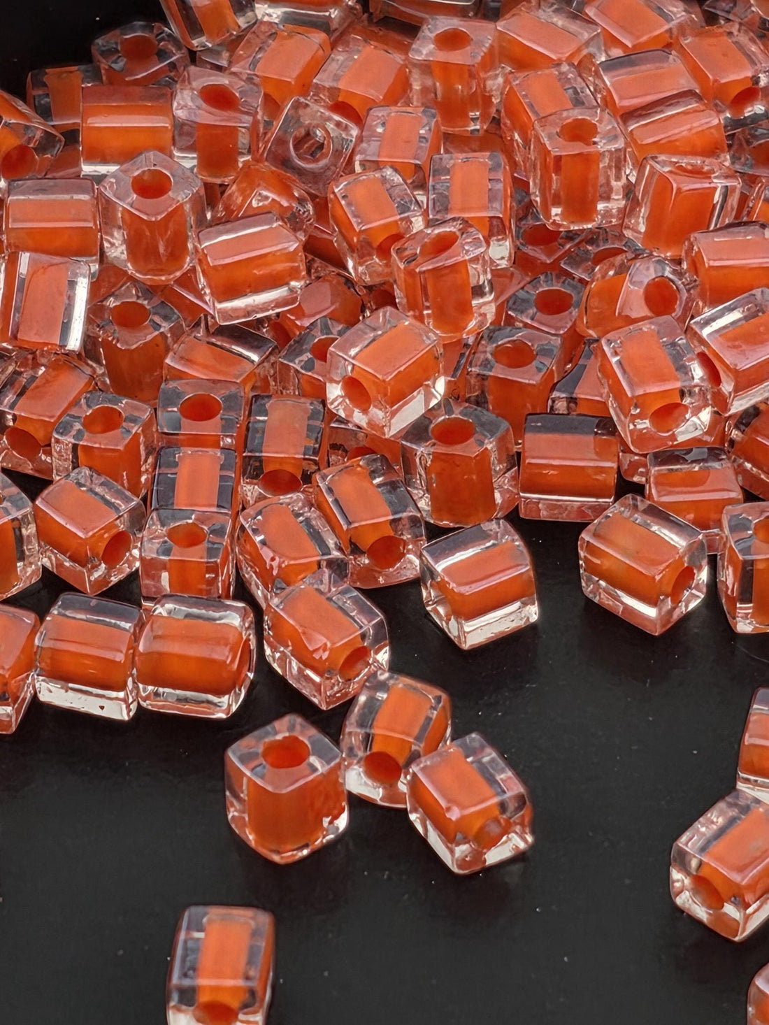 a close-up view of numerous small, clear plastic beads in shades of orange and red, scattered across a dark background.