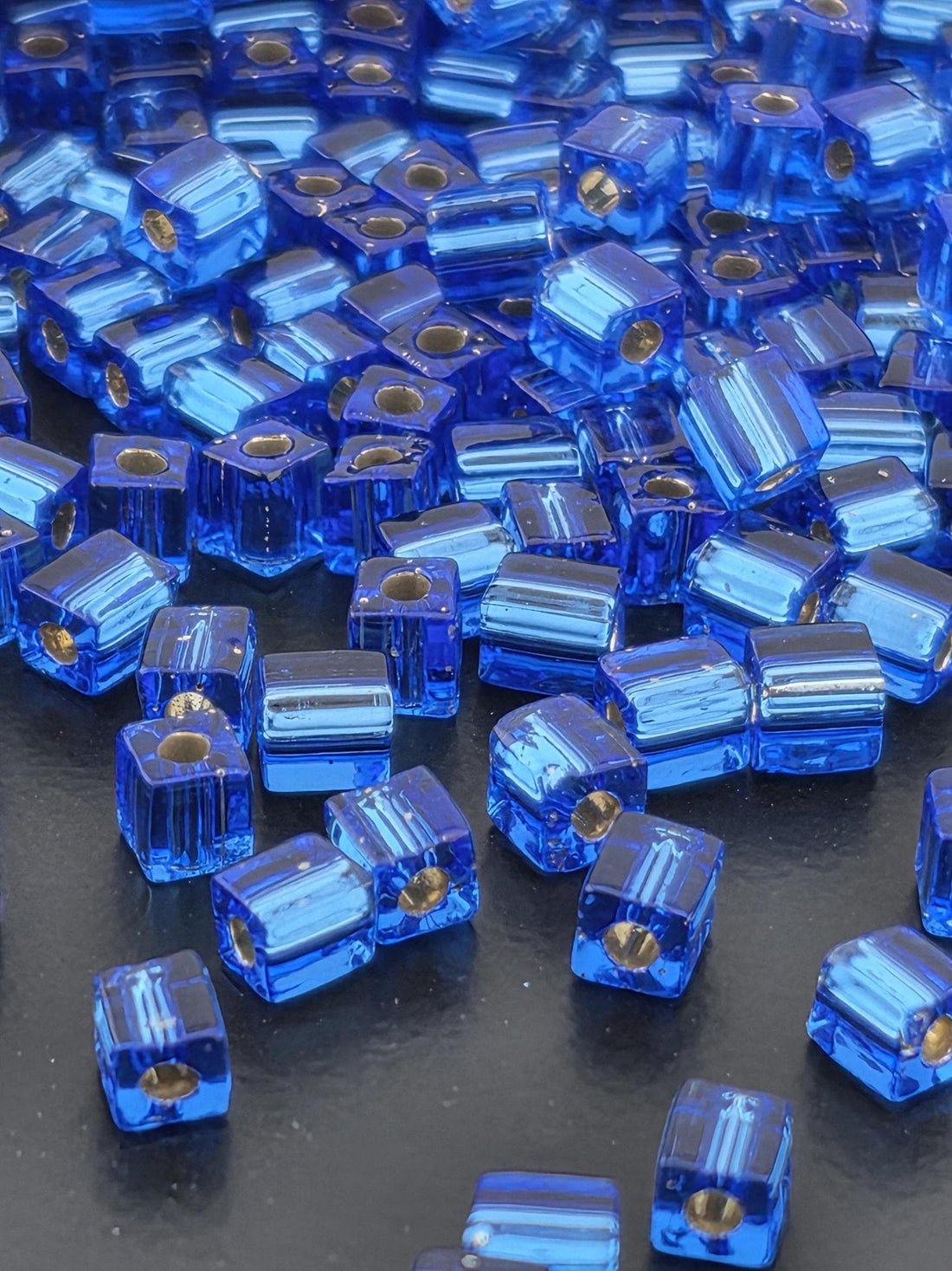 a close-up view of numerous blue and gold-colored glass beads scattered on a dark surface.