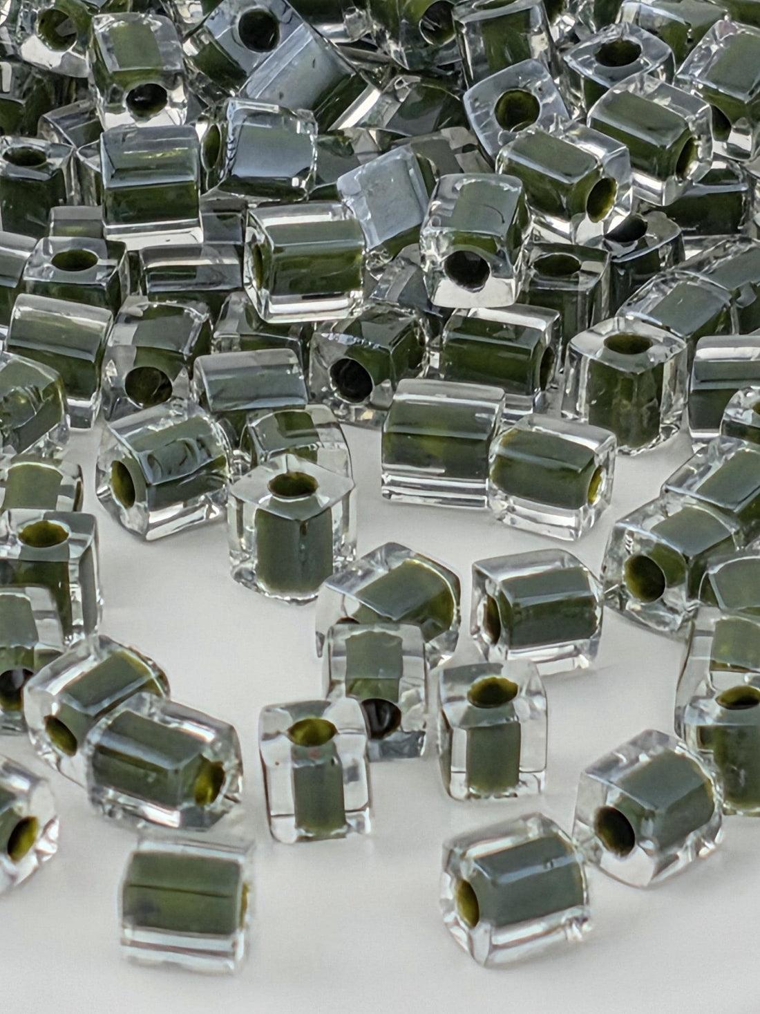 numerous transparent glass beads in various shades of green, scattered across a white background.