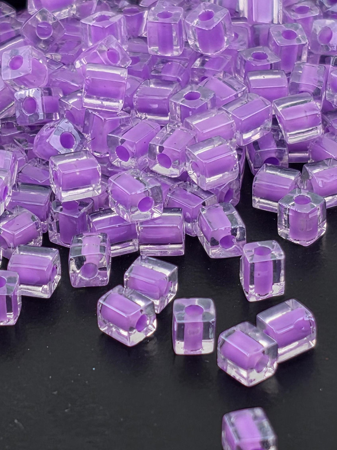 a close-up view of numerous clear, purple-colored glass beads scattered on a dark background.
