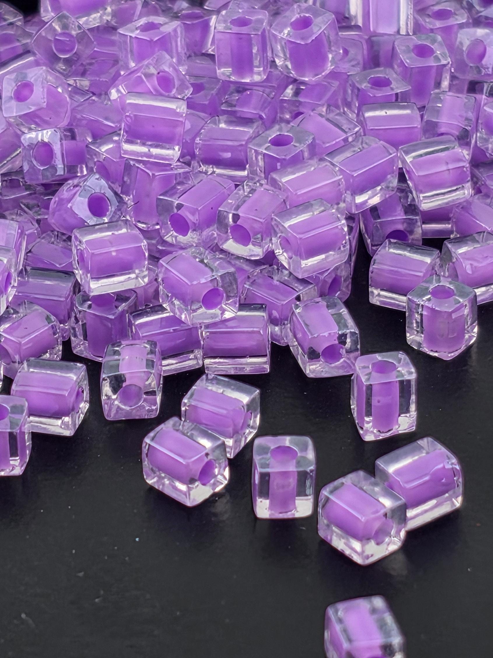 a close-up view of numerous clear, purple-colored glass beads scattered on a dark background.