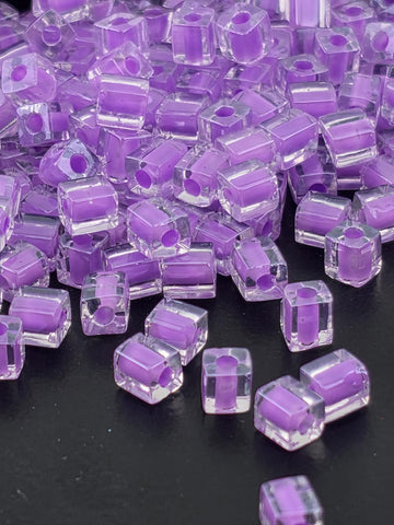 a close-up view of numerous clear, purple-colored glass beads scattered on a dark background.