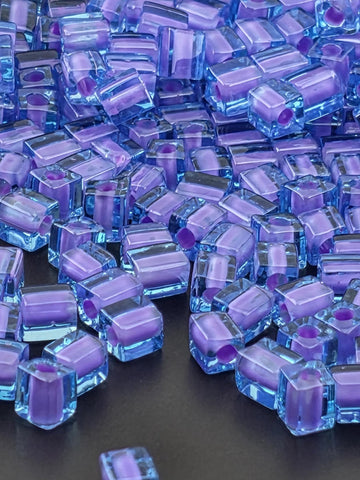 The image is a close-up of numerous small, clear, and purple-colored cubes or blocks arranged in a visually appealing manner.