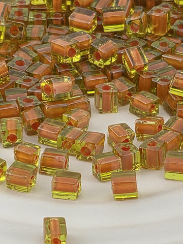 a close-up view of numerous small, clear glass beads in various shades of orange and yellow, scattered across a white surface.