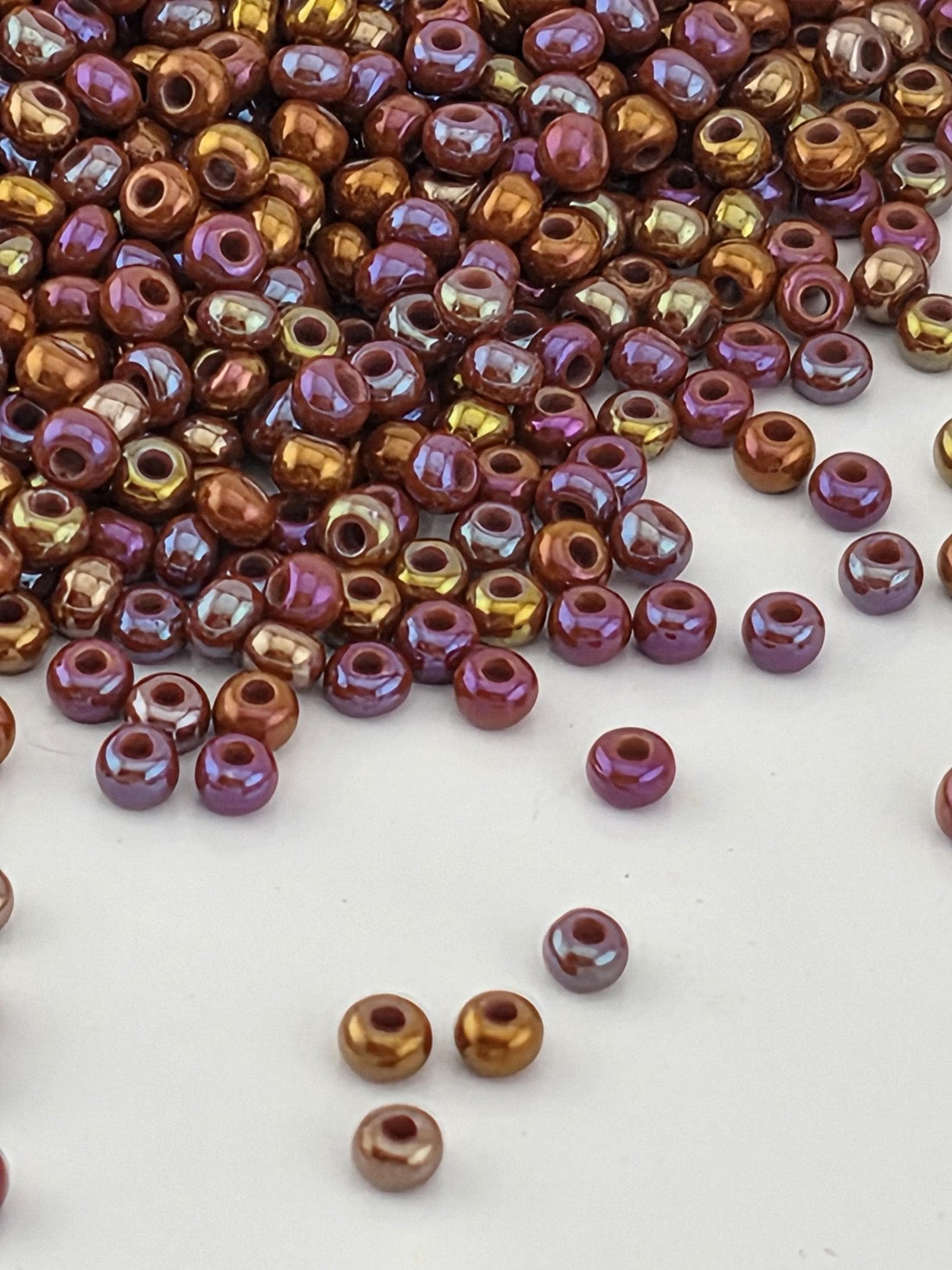 a collection of multicolored beads, including gold, purple, and brown, scattered on a white surface.