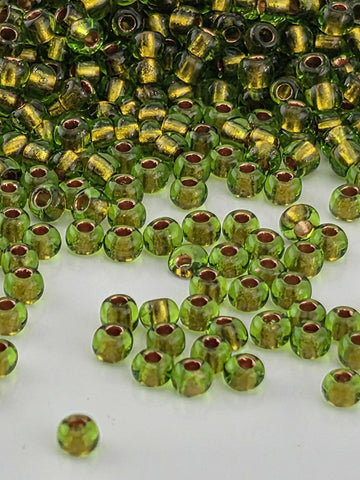 a collection of green and gold glass beads scattered on a white surface.