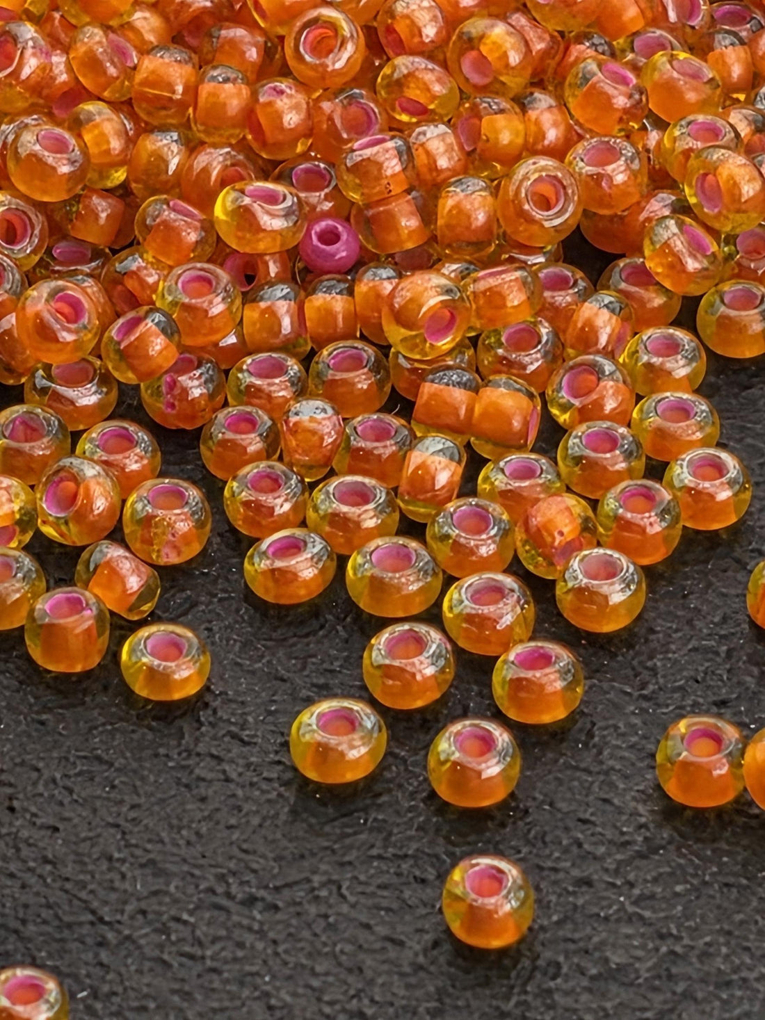 a collection of small, round, orange glass beads scattered on a dark surface.
