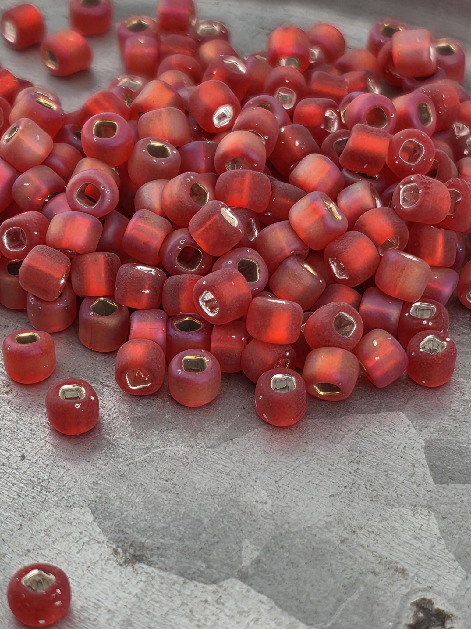 A pile of red glass beads with gold accents, scattered on a gray surface.
