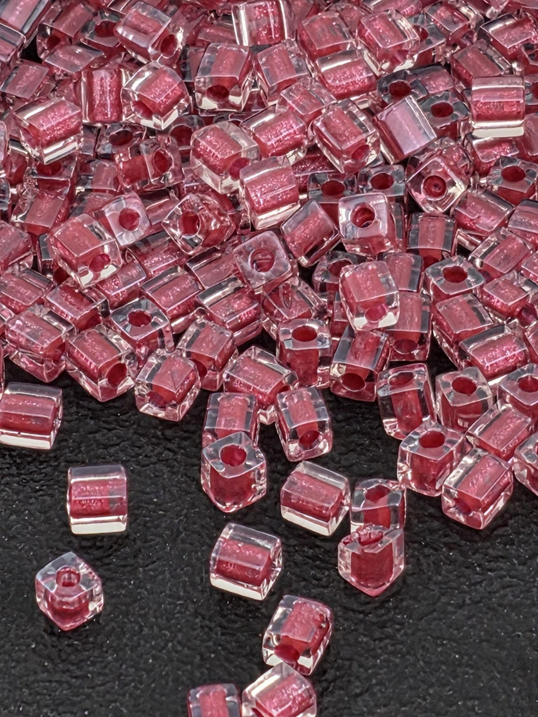 a close-up view of numerous clear, transparent beads in a pink color, scattered on a black surface.