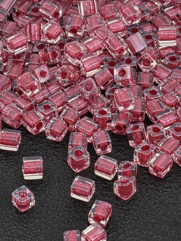 a close-up view of numerous clear, transparent beads in a pink color, scattered on a black surface.