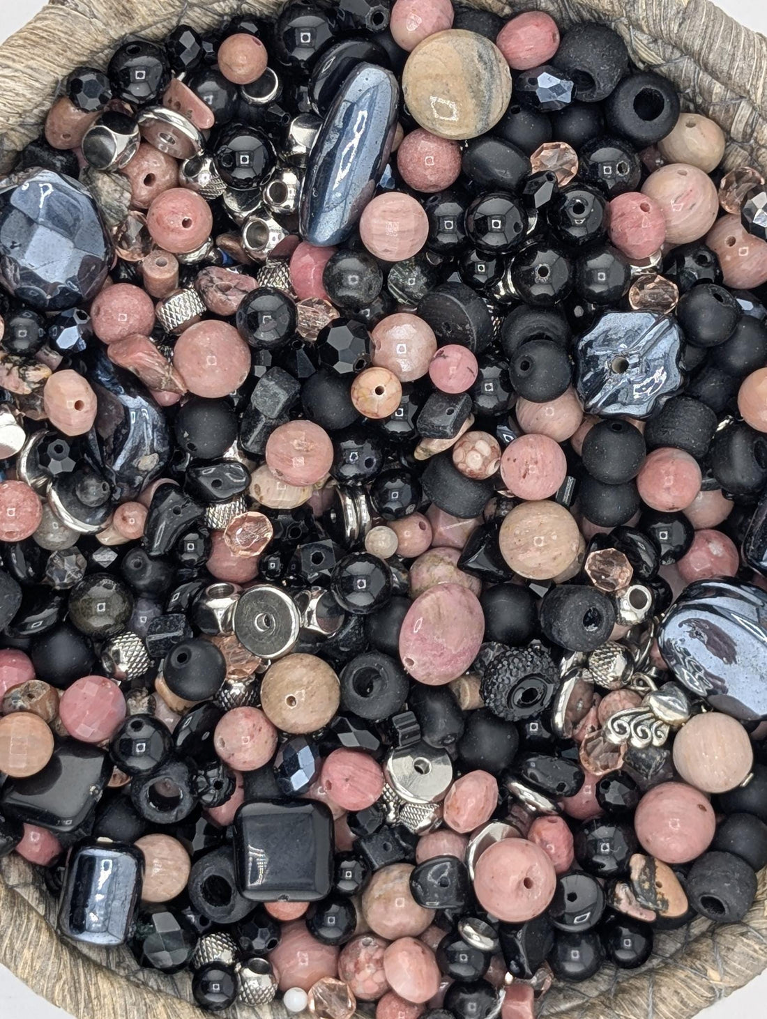 A collection of various beads, including black, pink, and multicolored beads, are scattered on a surface.