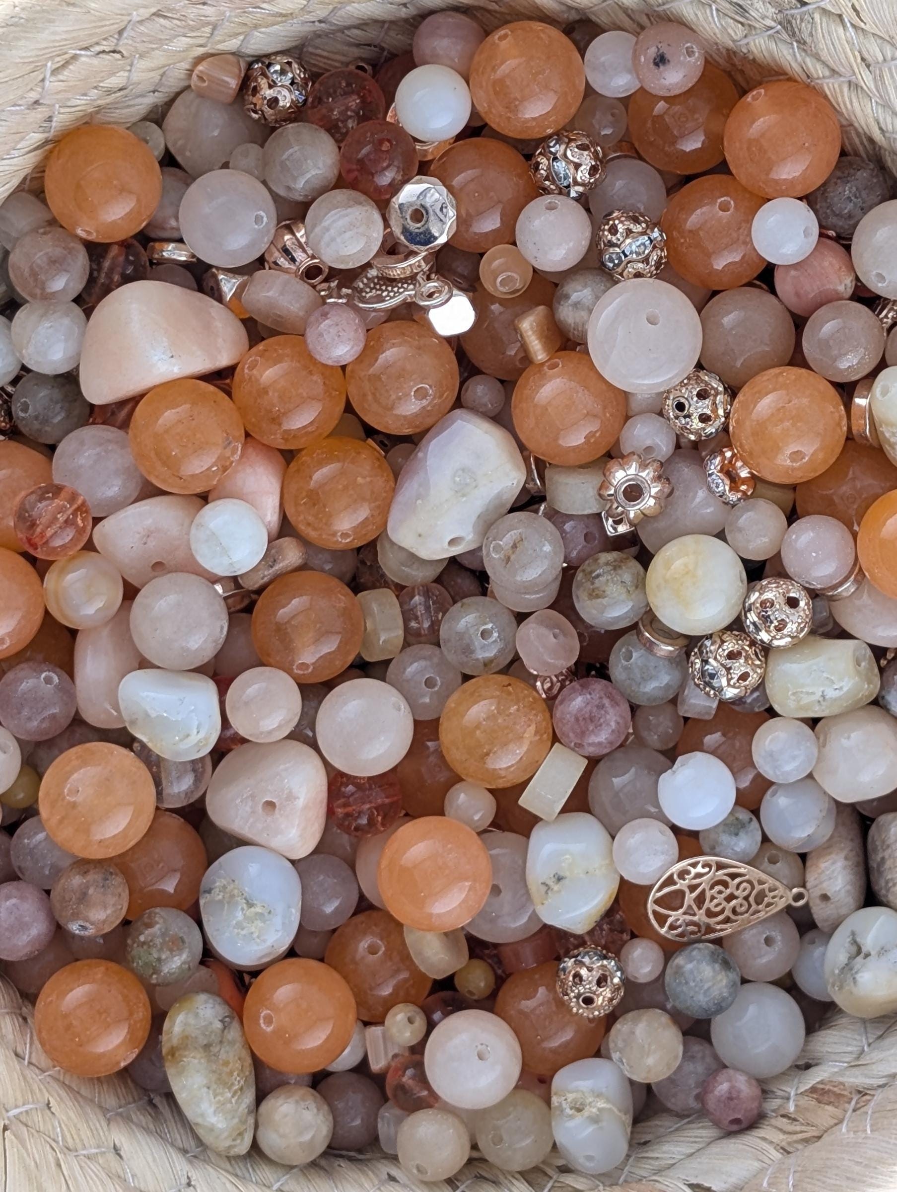 The image is a close-up of a variety of colorful beads and beads, including white, orange, and gold, arranged in a basket or container.