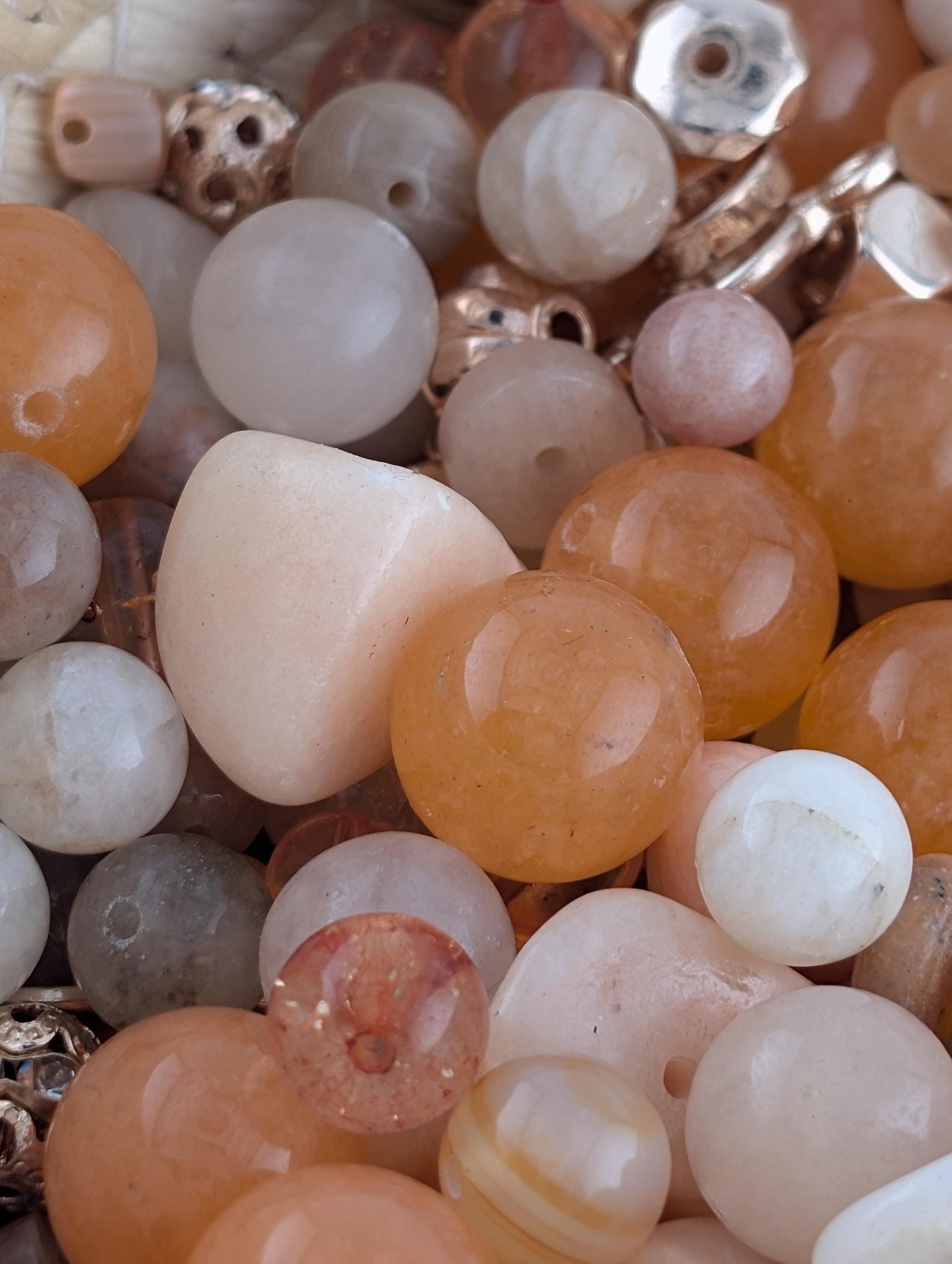 The image is a close-up of various beads and stones, including white, orange, and brown stones, as well as some glass beads.