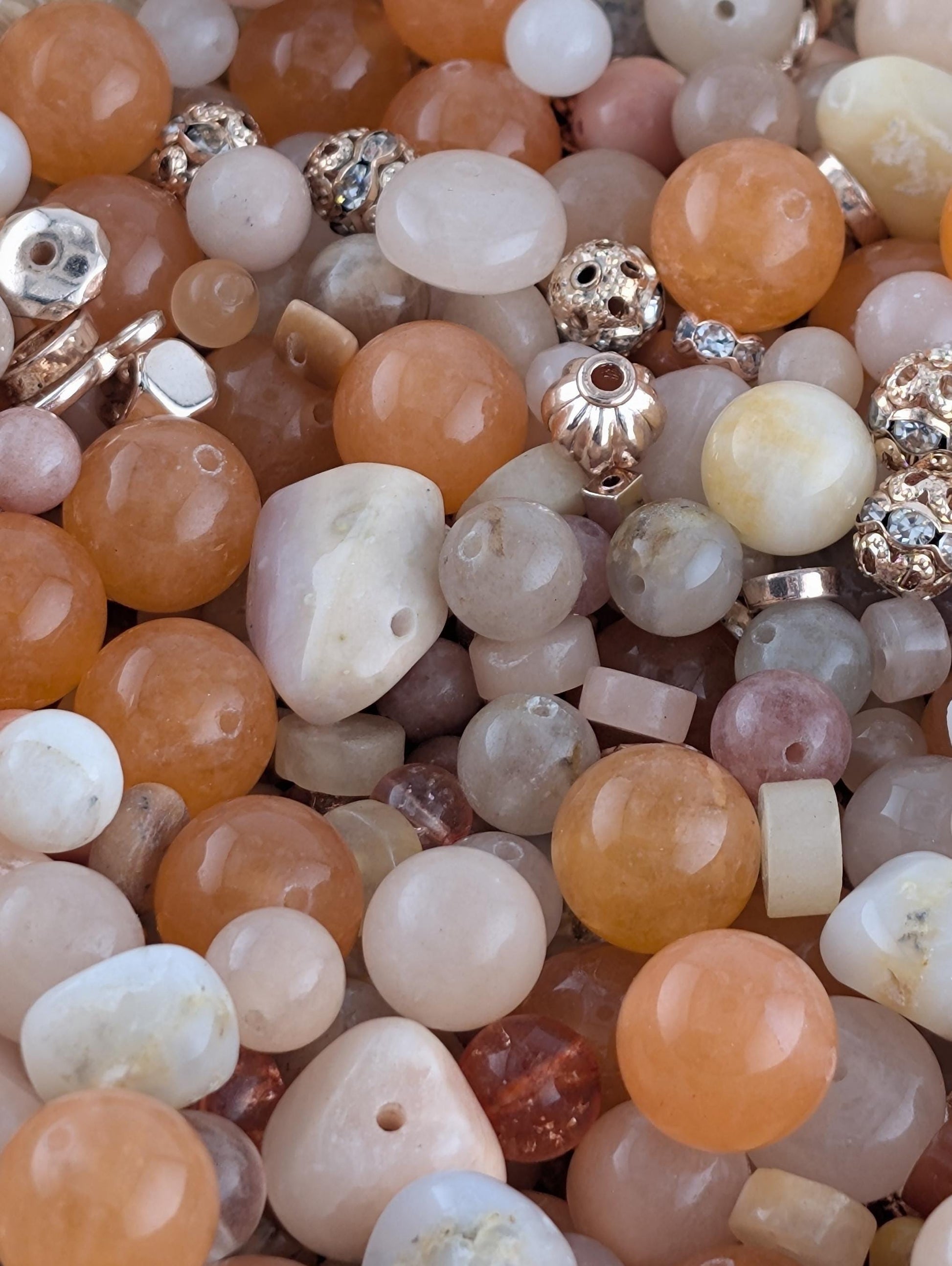 The image is a close-up of various beads and gemstones, including white, orange, and pink stones, as well as some with metallic accents.