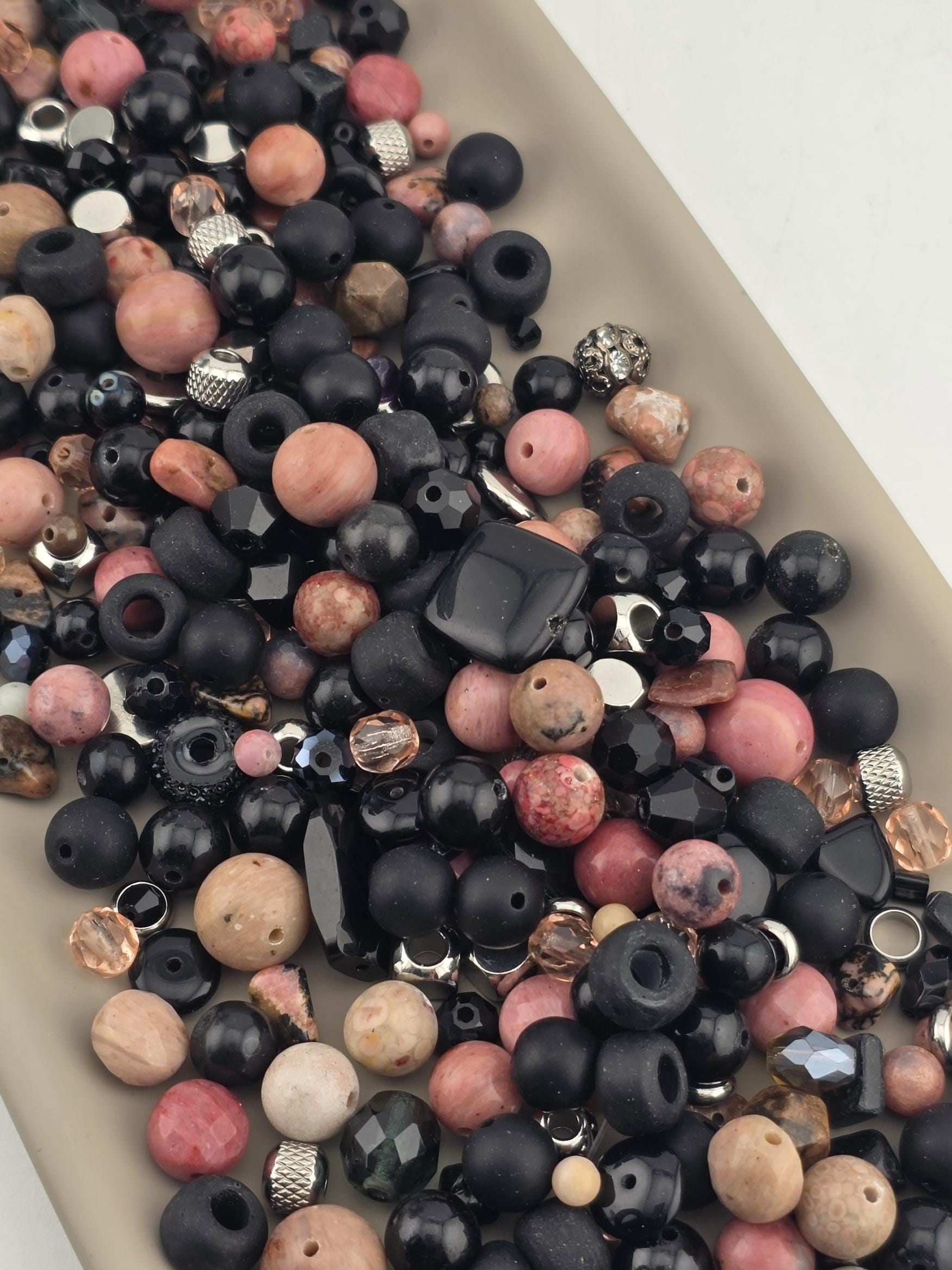 A collection of various beads, including black, pink, and multicolored beads, scattered on a surface.