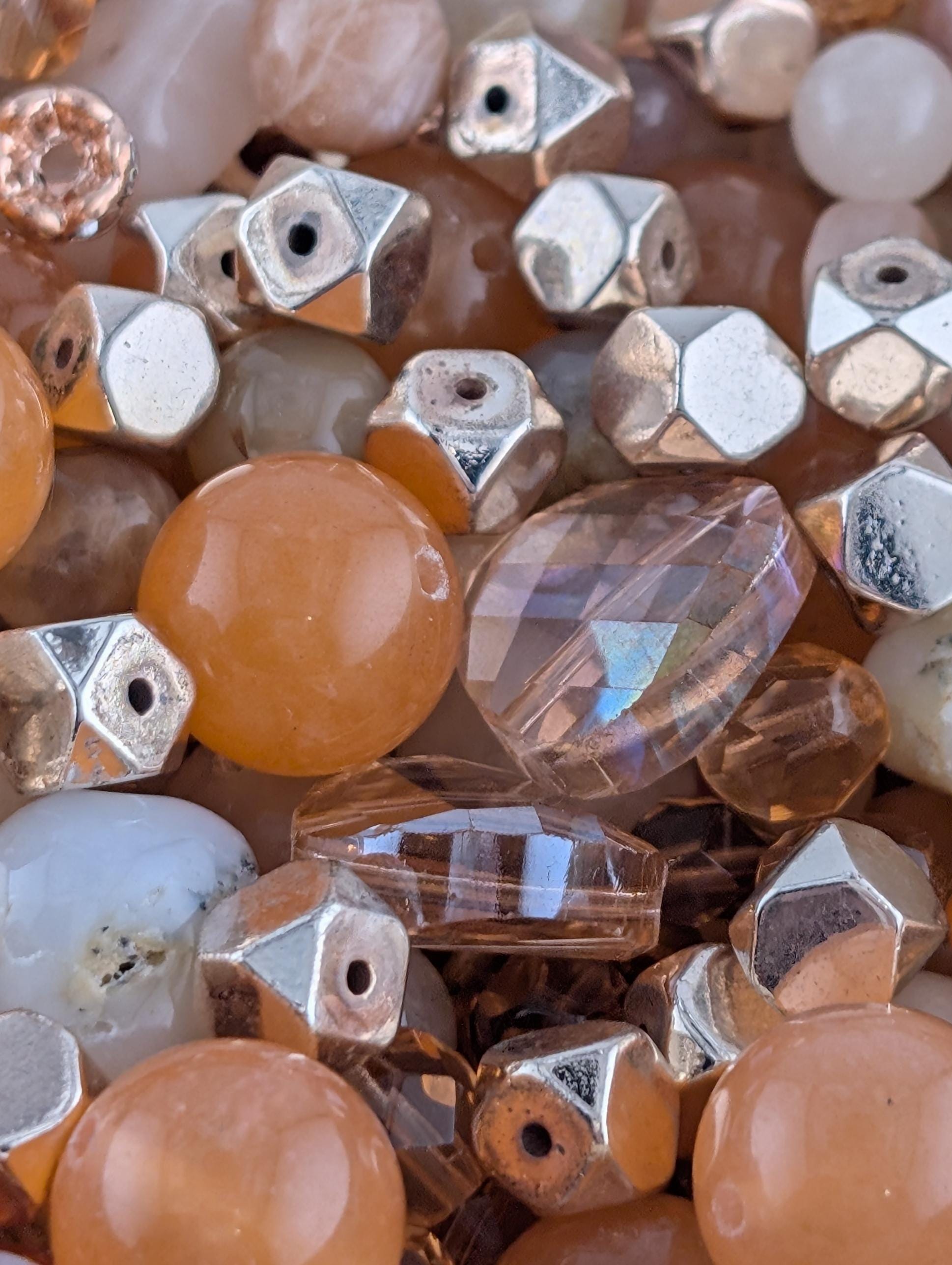 The image is a close-up of various beads and gemstones, including clear and multicolored glass beads, as well as some metallic and white beads.