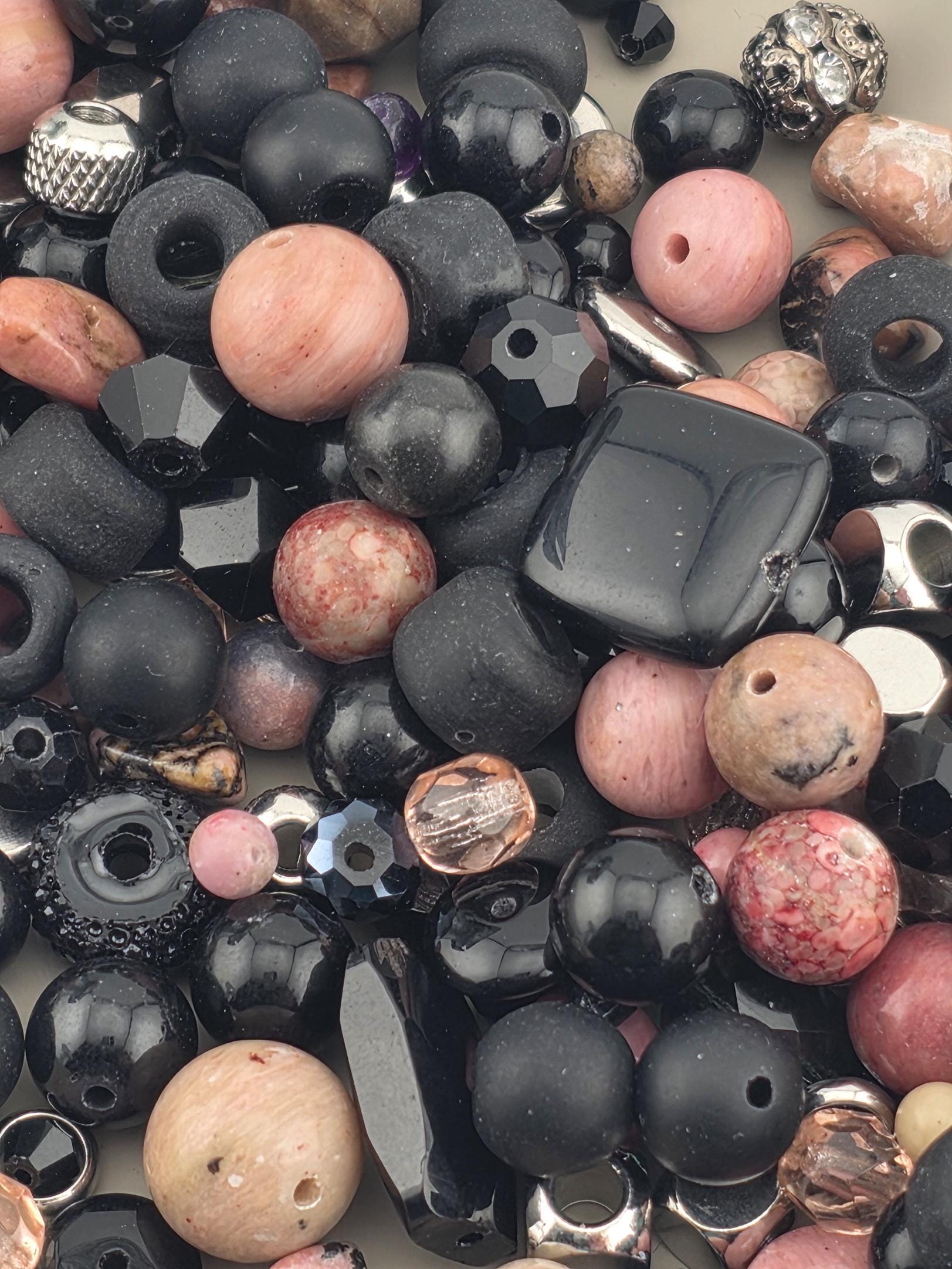 The image is a close-up of various beads and beads, including black, pink, and silver beads, scattered together.