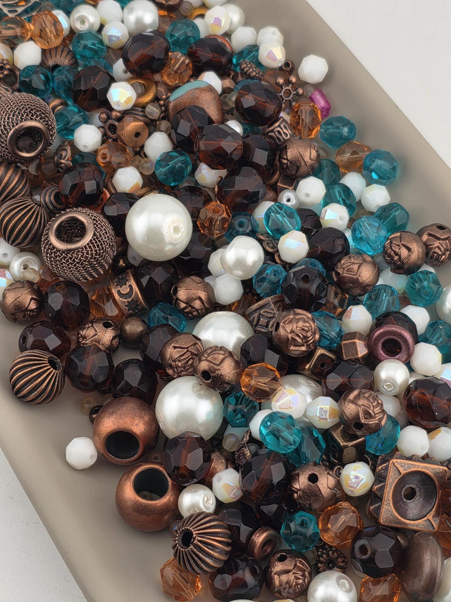 The image is a collection of various beads and beads in different shapes, sizes, and colors, including white, blue, brown, and copper-toned beads.