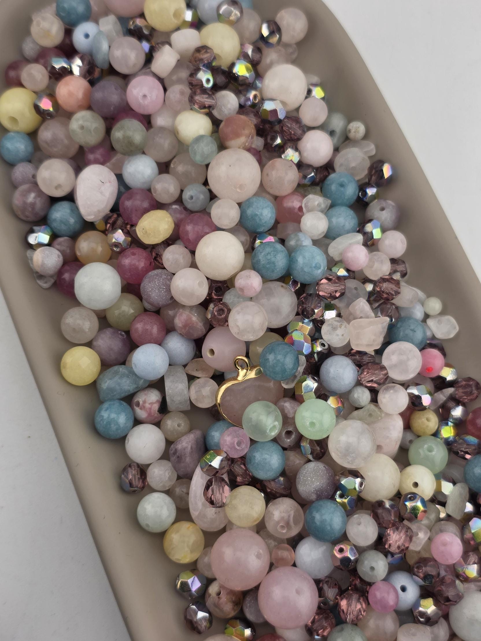 A collection of various colorful beads and gemstones, including clear, pink, blue, green, and multicolored stones, arranged on a surface.