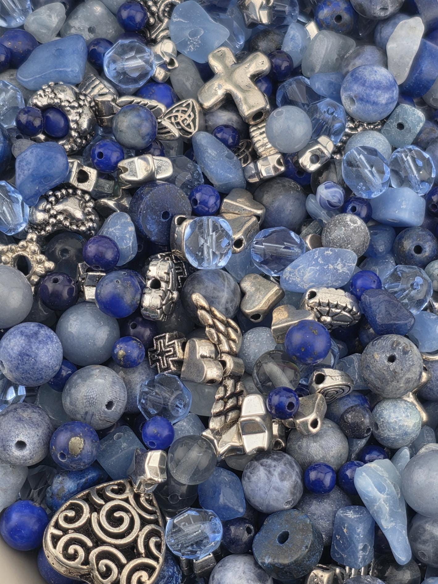 The image is a close-up of various beads and charms in shades of blue, silver, and gray, creating a visually appealing and diverse collection.
