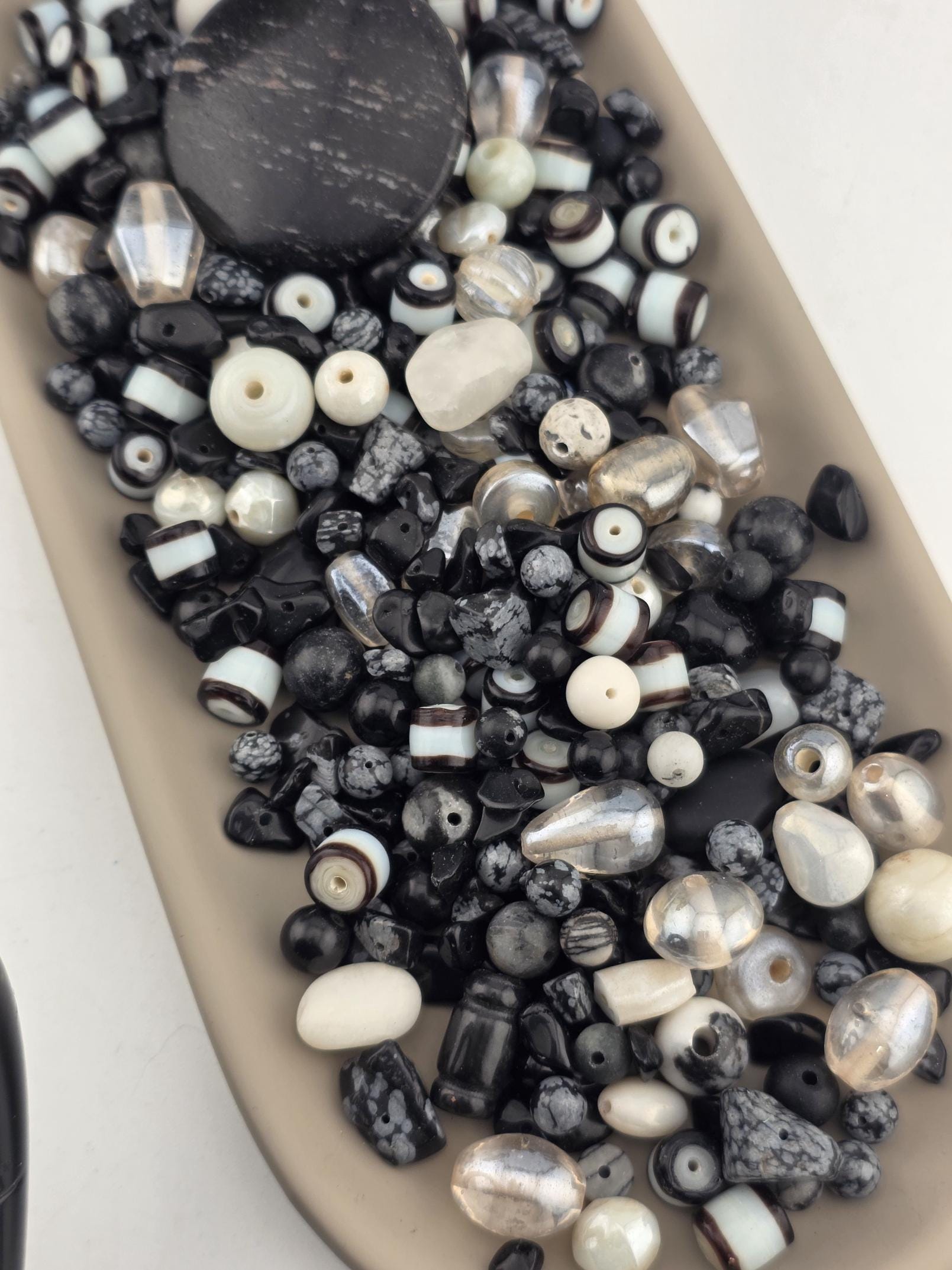 A collection of various beads in different shapes, sizes, and colors, including black, white, and silver beads, arranged on a surface.