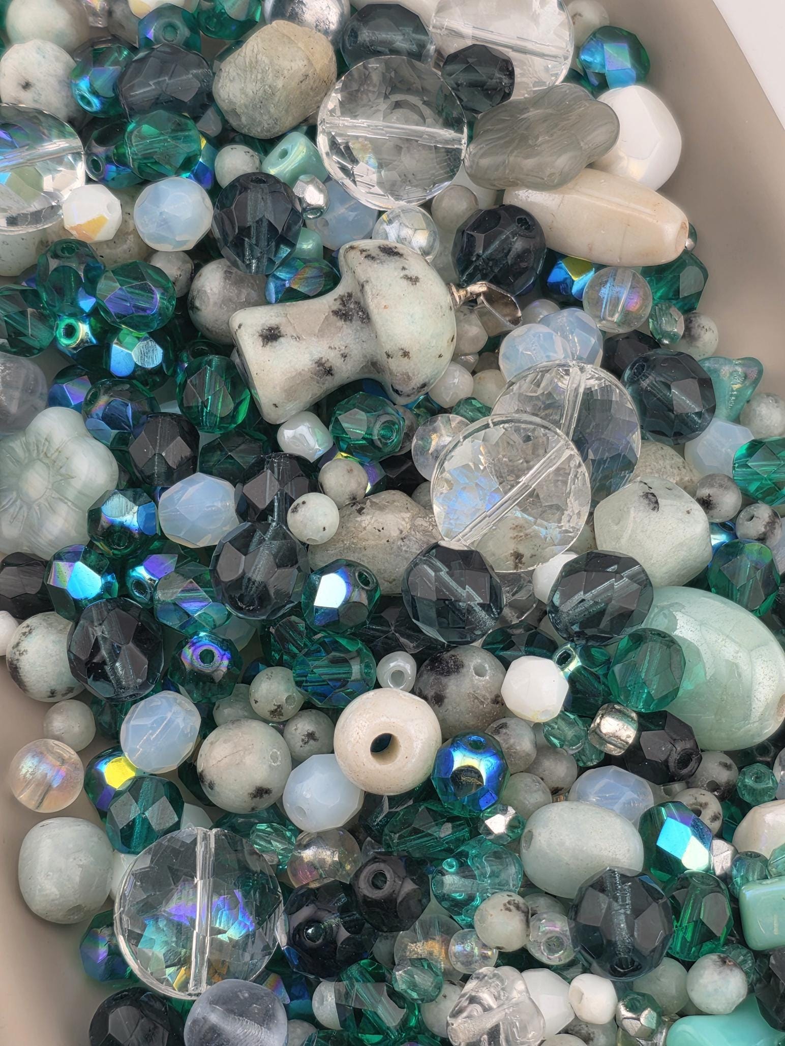The image is a collection of various colored glass beads, including clear, white, blue, green, and black beads, arranged in a visually appealing manner.