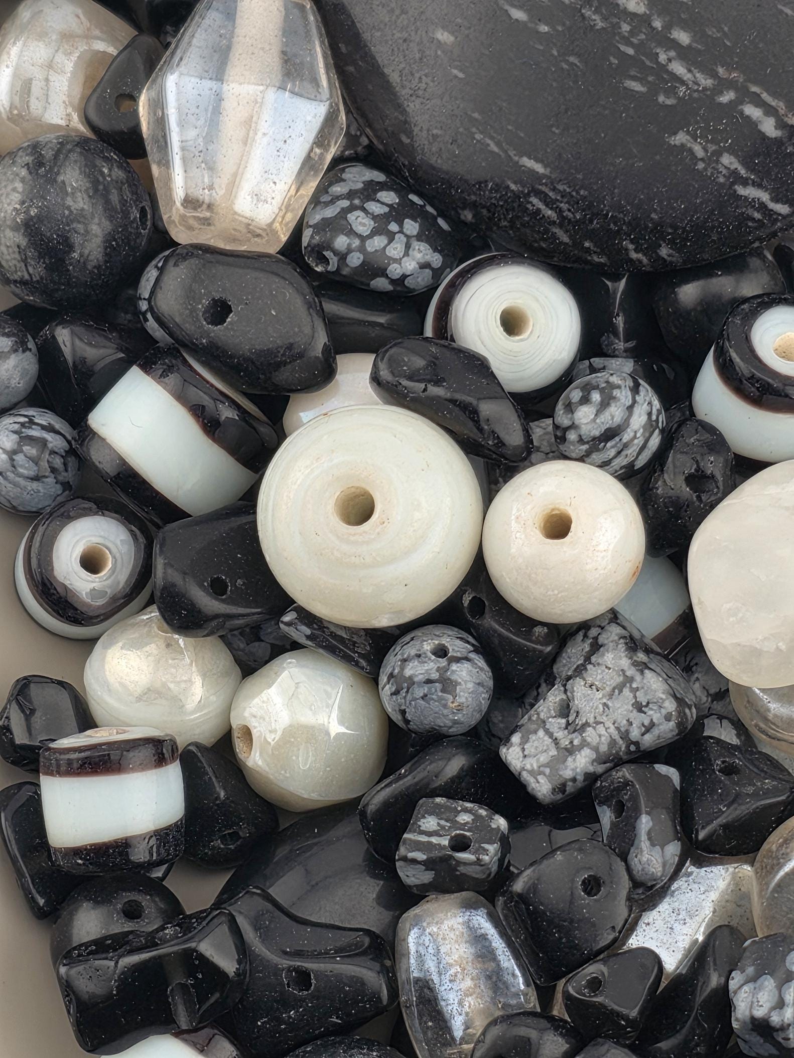 a collection of various beads and stones in shades of black, white, and gray, scattered together.